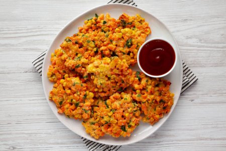 Téléchargez les photos : Beignets de maïs aux carottes faits maison avec ketchup sur une assiette, vue sur le dessus. Couché plat, au-dessus, d'en haut. - en image libre de droit