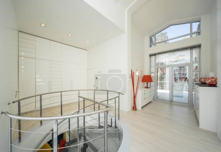 Photo for Modern interior of hall in luxury private house. Spiral staircase made of glass and metal. White wardrobe. - Royalty Free Image