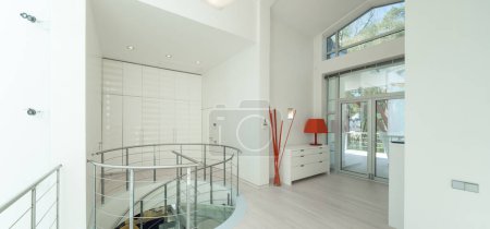 Photo for Modern interior of hall in luxury private house. Spiral staircase made of glass and metal. White wardrobe. - Royalty Free Image