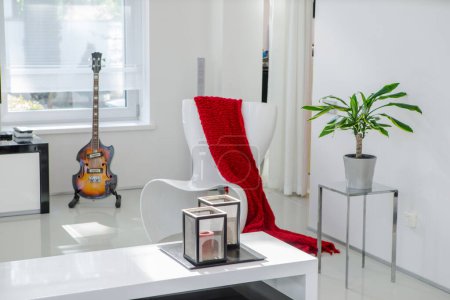 Photo for Modern white interior of luxury apartment. Living room. Chair, red plaid, guitar, green plant, candles. - Royalty Free Image