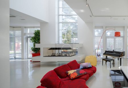 Modern interior of luxury private house. Spacious living room with red sofa, piano, white table.