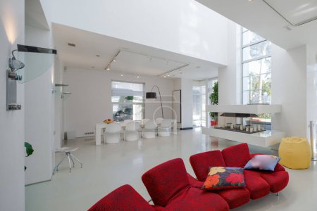 Foto de Interior moderno de la casa privada de lujo. Amplio salón con mesa y sillas. Paredes blancas. Sofá rojo. - Imagen libre de derechos