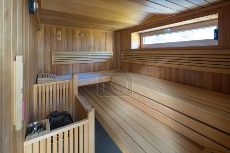 Foto de Moderno nterior de sauna finlandesa de madera. Piedras en la estufa eléctrica. Ventana pequeña. - Imagen libre de derechos