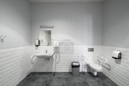 Das Innere des Badezimmers mit Einrichtungen für Behinderte. Weiße Ziegel. Graue Fliese.
