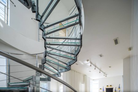 Téléchargez les photos : Intérieur moderne de maison privée de luxe. Gros plan de l'escalier en colimaçon en verre et métal. Murs blancs. - en image libre de droit