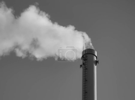 Foto de Chimenea de fábrica con humo. Tubo industrial. Cielo azul en el día soleado - Imagen libre de derechos