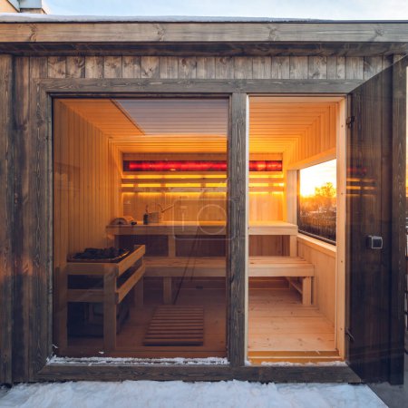 Small wooden finnish sauna with glass door on terrace of cottage. Luxury private house.