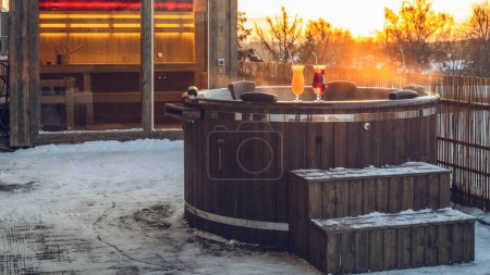 Hot outdoor wooden bath tub on terrace of private house at winter. Luxury cottage. Finnish sauna.