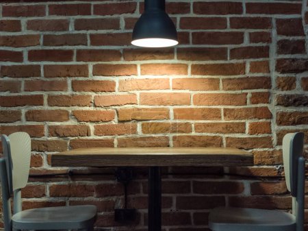 Foto de Lámpara cerca de una pared de ladrillo. Mesa y sillas de madera. Loft interior de café. - Imagen libre de derechos