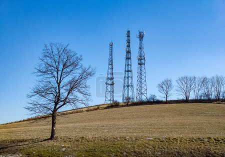 Foto de Torres de telecomunicaciones en el campo. Transmisor de antena de comunicación inalámbrica. Cielo azul en el fondo. Árbol. - Imagen libre de derechos