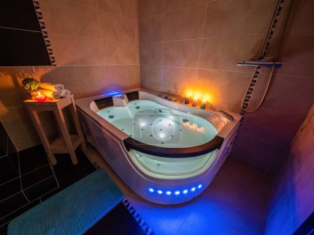Foto de Moderno interior de baño de lujo en apartamento. Baño de masaje iluminado con agua. Velas. Ambiente romántico. - Imagen libre de derechos