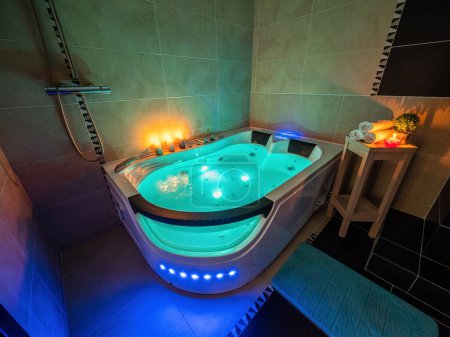Modern interior of luxury bathroom in apartment. Illuminated massage bath with water. Candles. Romantic atmosphere.