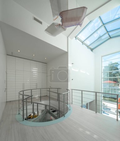 Modern interior of hall in luxury private house. Spiral staircase made of glass and metal. White wardrobe.