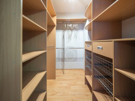 Photo for View of spacious empty wardrobe cloackroom in modern luxury apartment. Wooden shelves. - Royalty Free Image