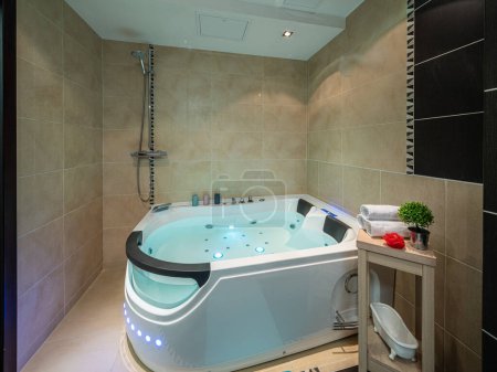 Modern interior of luxury bathroom in apartment. Illuminated massage bath with water. Toilet.