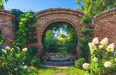 Foto de Hermoso jardín de verano en el día soleado. Césped verde, flores. Arck de ladrillo - Imagen libre de derechos