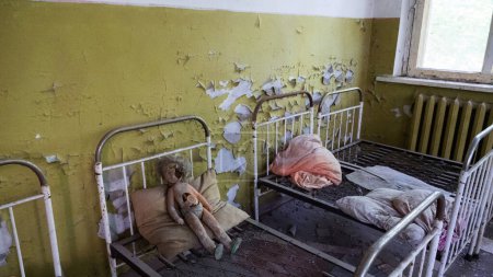 Foto de Muñeca de plástico en camas oxidadas en el jardín de infantes abandonado en la ciudad de Pripyat cerca de la central nuclear de Chernobyl. Zona radiactiva de exclusión, ciudad fantasma, Ucrania. Radiación, catástrofe - Imagen libre de derechos