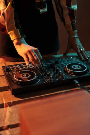 Woman disco jockey mixing sounds at dj turntables, using audio equipment to play music and do musical remix performance. Having fun with volume instrument, nightclub party. Close up.