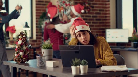 Photo for Festive people disturbing stressed woman during christmas time, feeling frustrated by noisy colleagues. Coworkers celebrating winter holiday season, interrupting tired person. Tripod shot. - Royalty Free Image