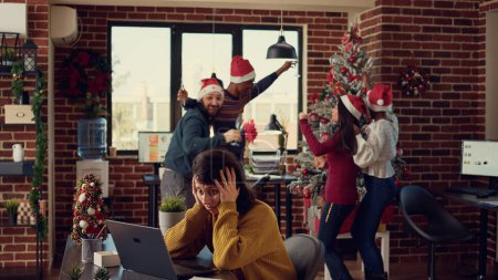 Photo for Angry frustrated person being interrupted by noisy people celebrating christmas holiday in startup office. Festive colleagues disturbing woman, making noise at work during winter season. - Royalty Free Image