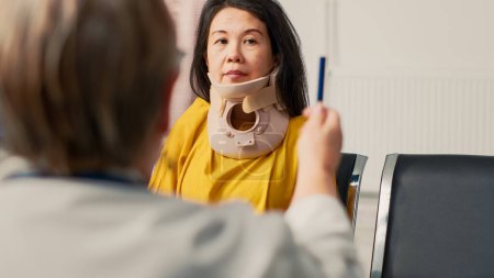 Médico consultando a paciente asiático con cuello cervical, revisando la vista y daño cerebral con luz. Especialista en salud que realiza consulta médica y examen en sala de espera.