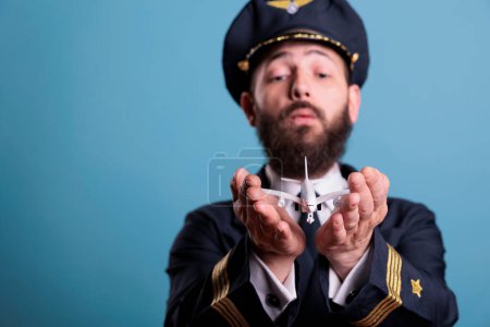 Photo for Airplane captain in uniform holding plane model in palms front view, pilot playing with commercial passenger jet toy. Professional aviation academy aviator on blue background - Royalty Free Image