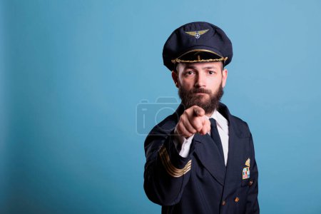Photo for Serious airplane aviator pointing at camera with finger, aviation academy pilot training recruitment. Confident finger wearing air crew uniform and hat front view portrait - Royalty Free Image