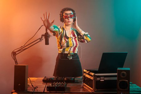 Modern musician doing stop sign with palm and listening to sounds in headphones, mixing music at turntables. Cool female DJ showing rejection and denial gesture, forbidden or refusal.