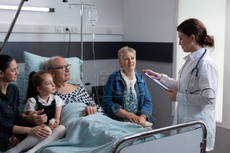 Geriatric physician performing routine medical examination of hospitalized elderly patient. Female general practitioner reporting health status of grandfather to family at hospital room.