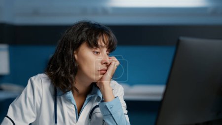 Photo for Tired doctor woman falling asleep while working late at night in hospital office, analyzing patient disease report on computer typing medical expertise. Stressed medic planning health care treatment - Royalty Free Image