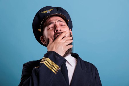Photo for Tired airplane aviator yawning closeup, exhausted pilot covering open mouth with hand. Sleepy aviation academy aircraft captain in aviation uniform with closed eyes front close view - Royalty Free Image