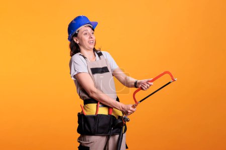 Téléchargez les photos : Femme experte en rénovation tenant une scie à main et utilisant une ceinture d'outils, travaillant sur un projet de rénovation. Rénovateur de bâtiment faisant le travail de menuisier avec scie à métaux et lame à trancher, travaux de rénovation. - en image libre de droit
