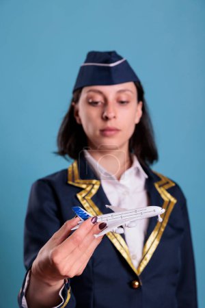 Photo for Young stewardess holding airplane model, aviation academy flight attendant playing, selective focus on plane. Air hostess looking at commercial jet toy, front view studio medium shot - Royalty Free Image