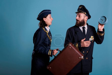 Photo for Flight attendant and pilot running late at airport, holding retro alarm clock, carrying suitcase. Airplane stewardess and airplane captain overslept, looking at time, hurry up at work with luggage - Royalty Free Image