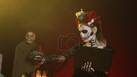 Photo for Female model doing online shopping on laptop, paying with credit card in studio. Making electronic payment transaction on pc, looking like holy goddess of death on halloween tradition. Handheld shot. - Royalty Free Image