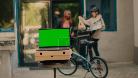 Photo for Laptop showing greenscreen display outdoors, food delivery service at front door. Running isolated chroma key template with blank mockup and copyspace background on computer screen. - Royalty Free Image