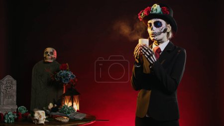 Photo for Woman with skull make up blowing burning candle in studio, being dressed as goddess of death to celebrate dios de los muertos. Putting out flame and acting creepy on traditional halloween. - Royalty Free Image