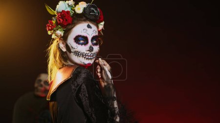 Photo for Cavalera catrina luring victims and reaching with hand, tempting and looking flirty on mexican halloween. Lady of death acting horror with skull make up and goddess costume. Handheld shot. - Royalty Free Image