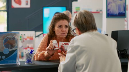 Photo for Female client showing cardiology pills to specialist, asking about medical support to buy treatment. Person looking at boxes of supplements and drugs to buy at pharmacy cash register. - Royalty Free Image