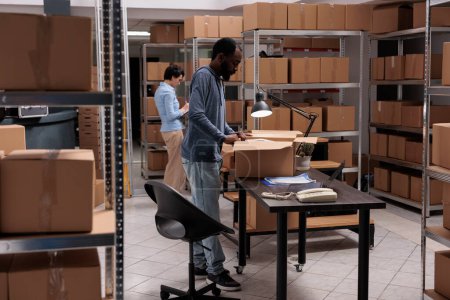 Photo for Storehouse manager preparing clients orders putting products in carton boxes, checking shipping details before delivery packages. Diverse team working in distribution center warehouse - Royalty Free Image