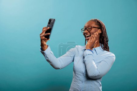 Photo for Excited pleased young adult person smiling at phone camera while taking picture for social media. Happy confident african american woman with modern touchscreen smartphone taking selfie photo. - Royalty Free Image