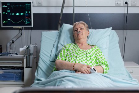 Photo for Female patient resting after surgery in hospital monitoring room. Elderly lady connected to medical equipment measuring vital signs. Old woman relaxing in sanatorium recovery bedroom. - Royalty Free Image