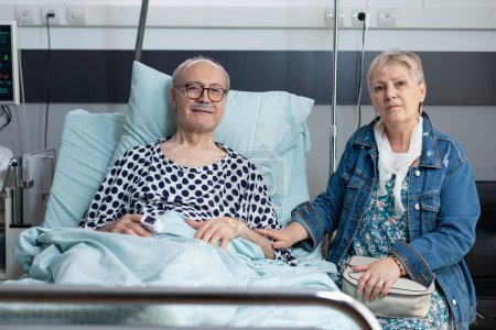 Photo for Elderly woman visiting sick husband in hospital room. Older couple looking at camera in geriatric clinic observation room. Senior lady accompanying recovering old man in sanatorium. - Royalty Free Image