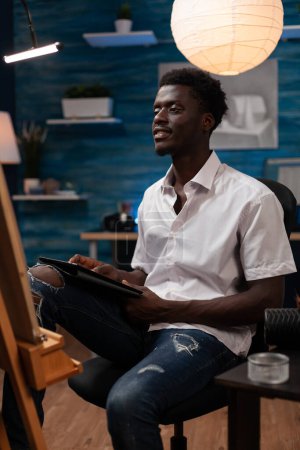 Photo for Portrait of drawing student reviewing artistic notes on tablet for assignment in home art studio. Young african american artist using a digital devise to look for inspiration to create sketch on - Royalty Free Image