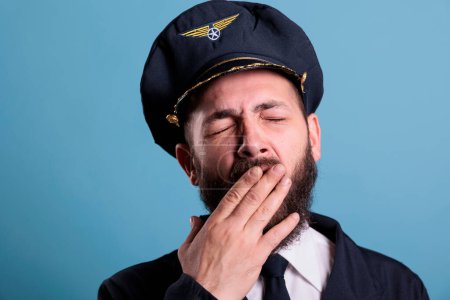 Photo for Tired airplane pilot yawning closeup, exhausted aviator covering open mouth with hand. Sleepy aviation academy aircraft captain in uniform with closed eyes front close view - Royalty Free Image
