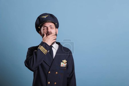 Photo for Tired airplane pilot yawning, covering open mouth with hand, exhausted aviator. Sleepy aviation academy plane captain in uniform with closed eyes front view, studio medium shot - Royalty Free Image