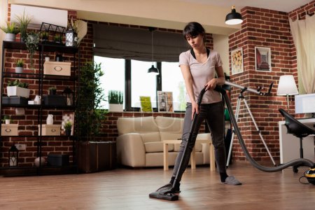 Photo for Wife takes care of spring cleaning, vacuums the dust in the living room at home. Housewife in slippers does home chores with dedication, tidies and cleans the whole place. - Royalty Free Image