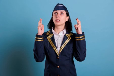 Photo for Flight attendant crossing fingers, looking up, praying for luck before flying. Superstitious stewardess in uniform getting lucky, pleading for success with hopeful facial expression - Royalty Free Image