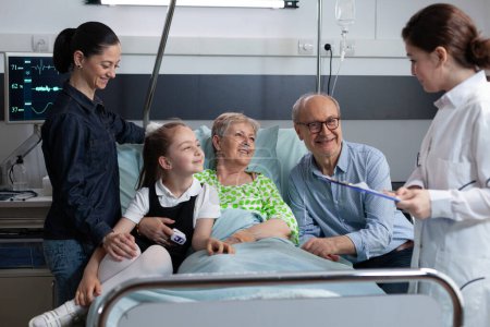Photo for Hospital medical staff member informing elderly female patient family of positive surgical outcome. Healthcare professional checking elderly patient activity in geriatric clinic room. - Royalty Free Image