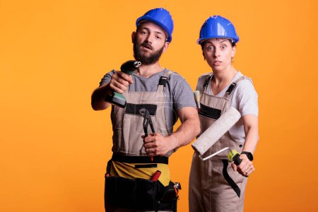 Photo for Professional renovators showing construction tools in studio shot, holding mutiple working instruments. Team of constructors working with pair of pliers, power drill gun, roller and paintbrush. - Royalty Free Image